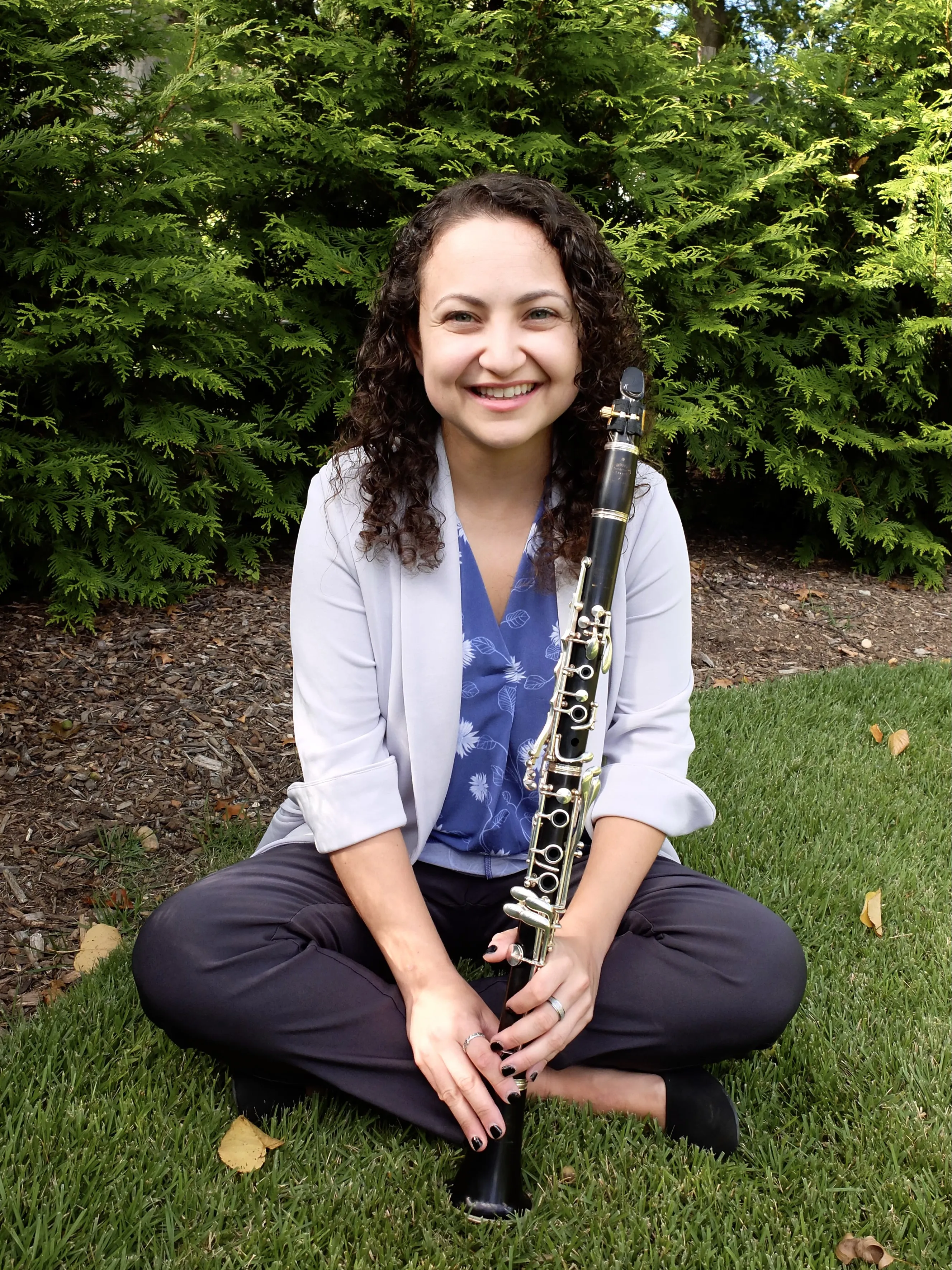 Valerie sitting criss-cross applesauce with her clarinet in the grass with a big smile