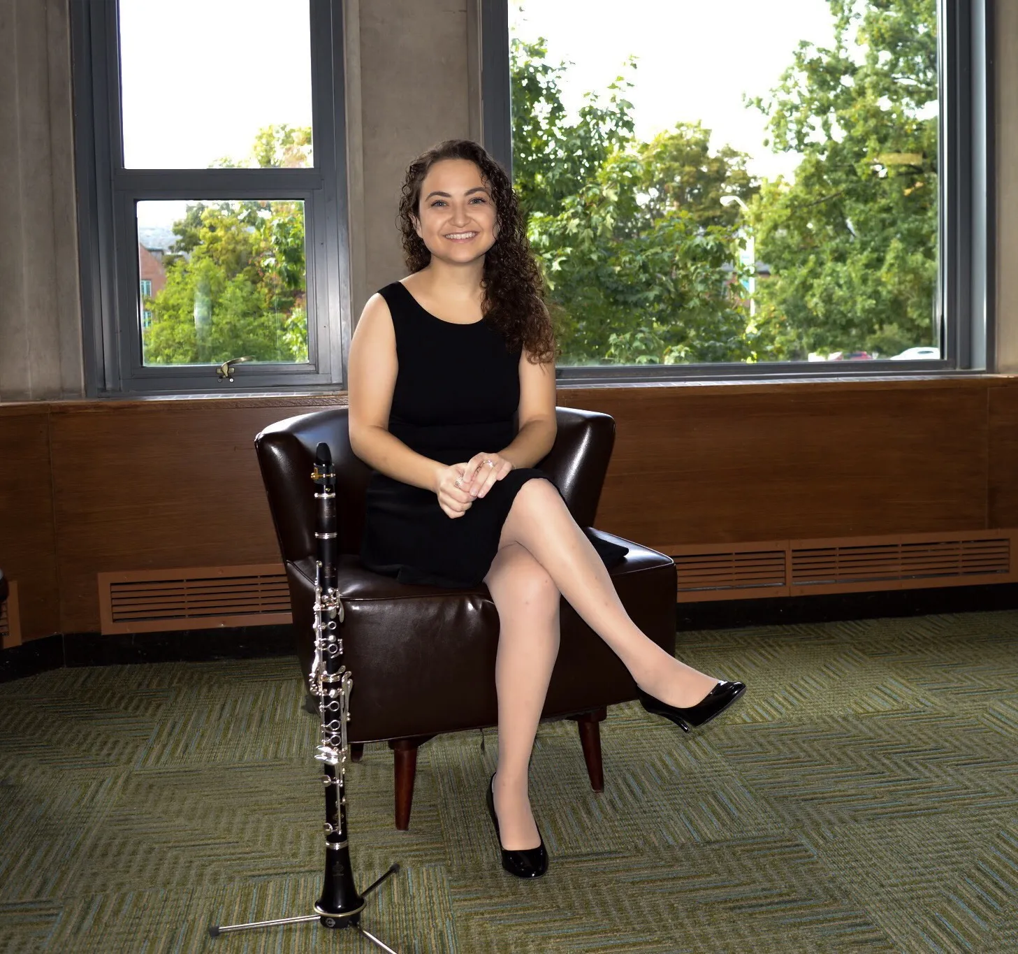 valerie smiling with a black dress on, sitting in a chair with her clarinet on a stand in front of her