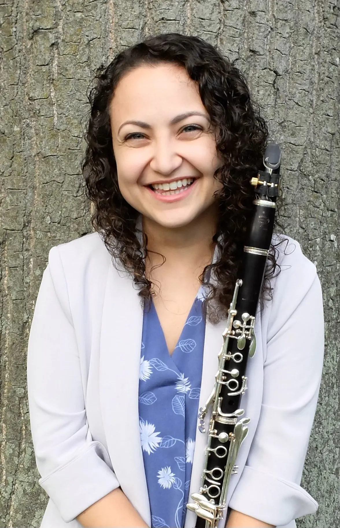 A close-up of Valerie against a large tree, smiling while holding her clarinet