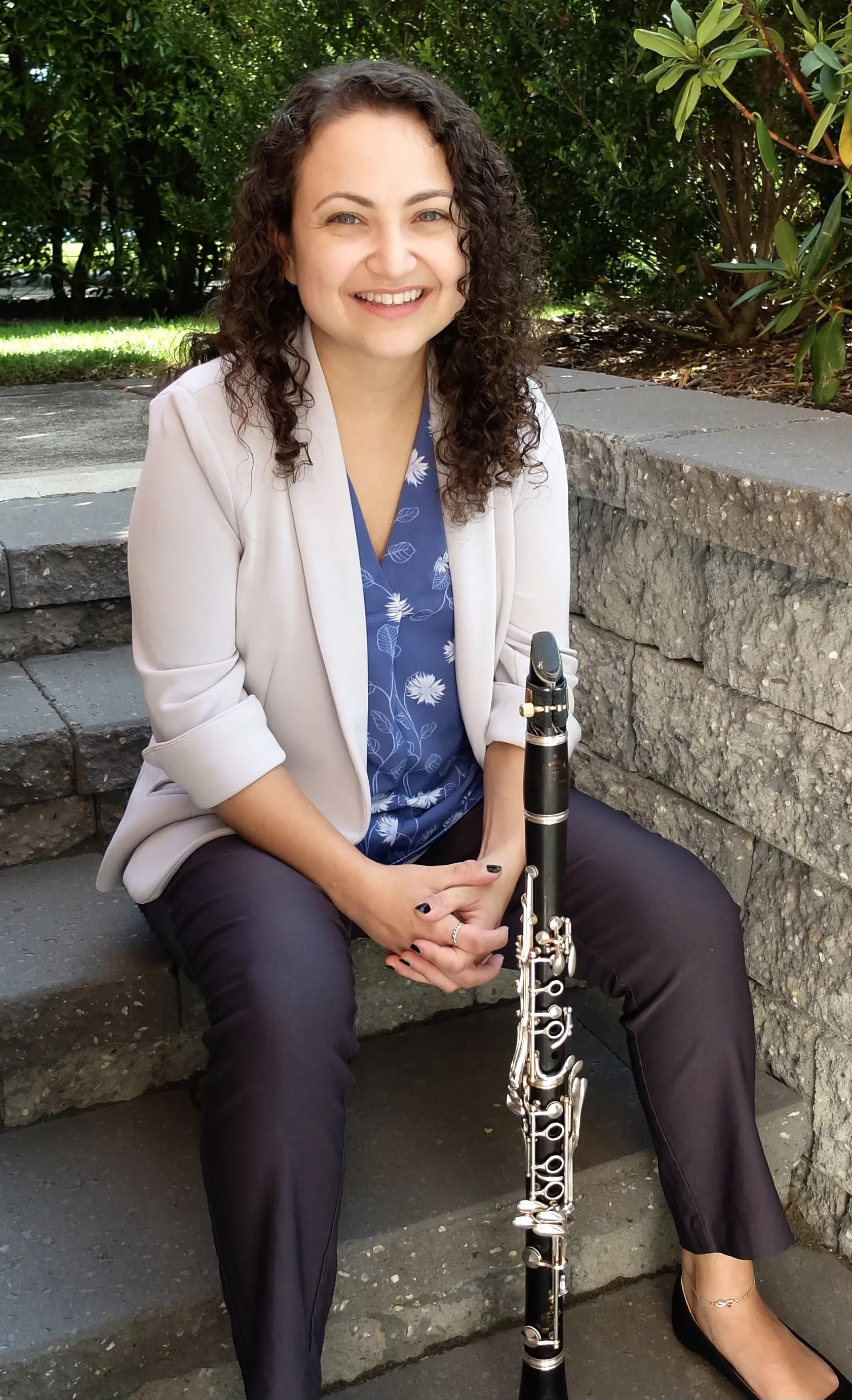 Valerie smiling and sitting on stone steps with her clarinet standing in front of her