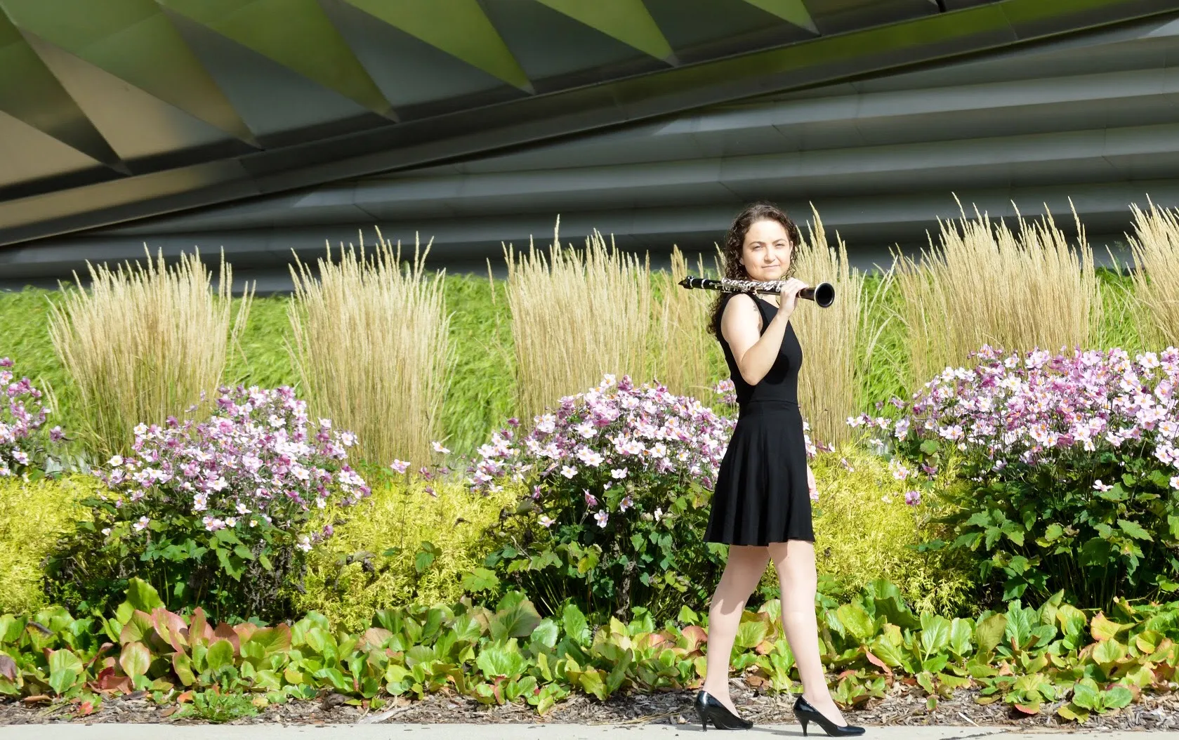 Valerie walking with her clarinet over her shoulder, in front of a garden